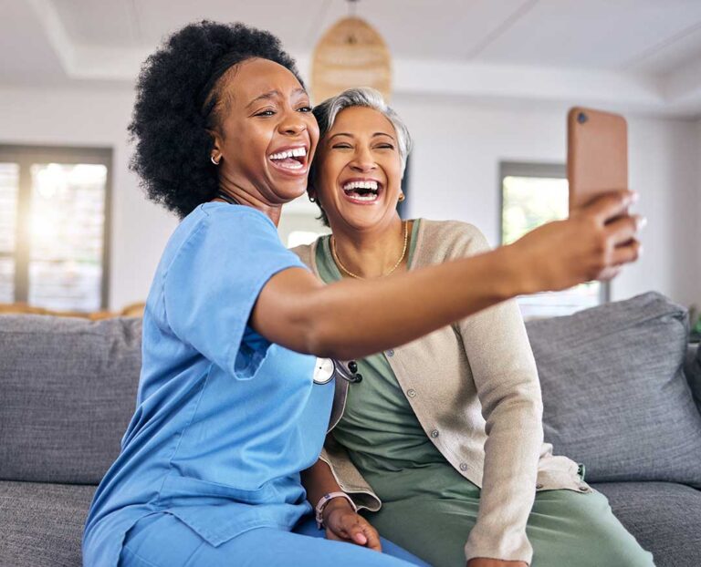 A senior woman and caregiver talking at a table in a well-lit, comfortable communal living space.